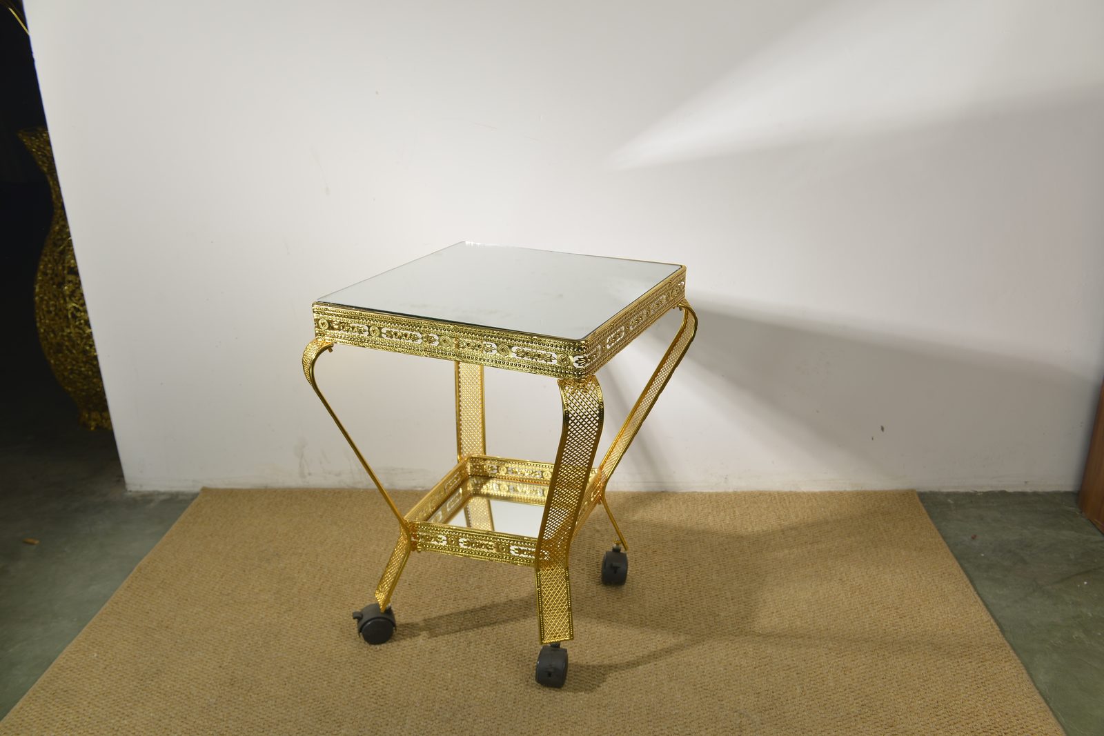 Gold metal serving trolley with lattice legs and rolling wheels
